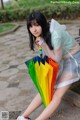 A woman sitting on a bench holding a rainbow colored umbrella.