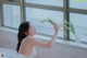 A woman in a white dress holding a flower in front of a window.