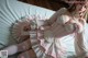 A woman in a pink and white dress sitting on a bed.