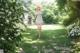 A woman walking through a lush green park with white flowers.