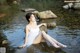 A woman in a white dress sitting on a rock in the water.