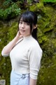 A woman standing in front of a moss covered wall.