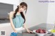 A woman in a blue top and white apron cleaning a kitchen counter.